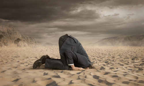 Young businessman hiding head in the sand